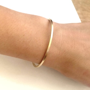 May include: A simple gold bangle bracelet on a person's wrist.