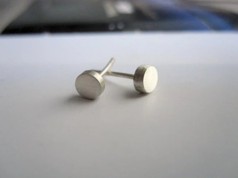 May include: A pair of silver stud earrings with round, flat tops.