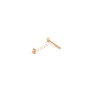 May include: A pair of gold square stud earrings. The earrings are small and delicate, with a simple design.