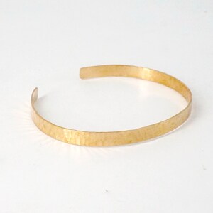May include: A simple gold hammered bangle bracelet. The bracelet is made of a single piece of metal that is bent into a circle.