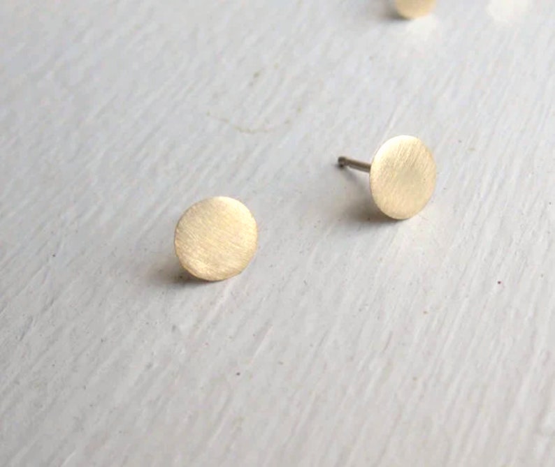 Puede incluir: Un par de pendientes de bot&oacute;n dorados con un dise&ntilde;o circular. Los pendientes tienen un acabado cepillado.