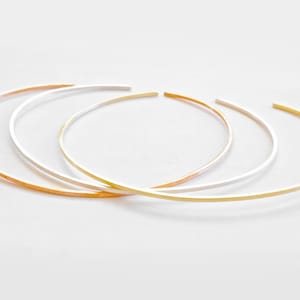 May include: Three thin metal bangles in gold, silver, and rose gold.