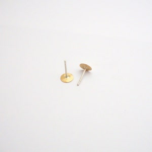 May include: A pair of gold-toned stud earrings with silver posts. The earrings are round and have a smooth, slightly textured surface.