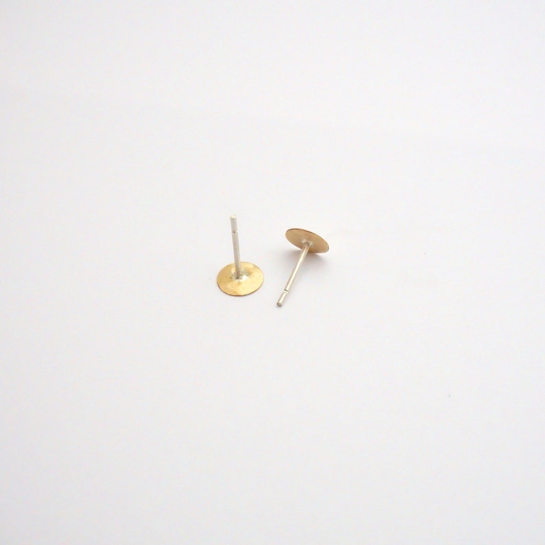 May include: A pair of gold-toned stud earrings with silver posts. The earrings are round and have a smooth, slightly textured surface.