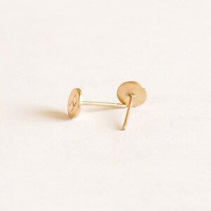 May include: A pair of gold-toned stud earrings with a round shape. The earrings are simple and minimalist.