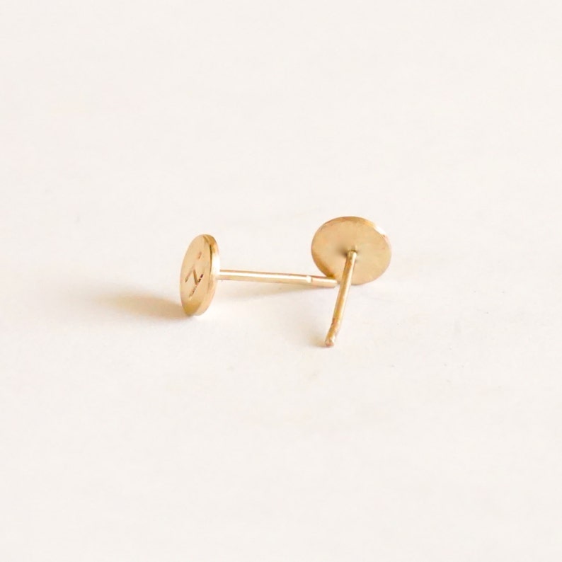May include: A pair of gold-toned stud earrings with a round shape. The earrings are simple and minimalist.