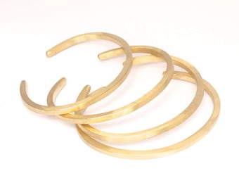 May include: Four gold-toned metal bangles stacked on top of each other. The bangles are simple and have a smooth, polished finish.