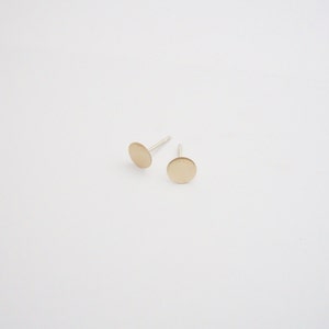 May include: A pair of gold-toned stud earrings with a circular design. The earrings are on a white background.