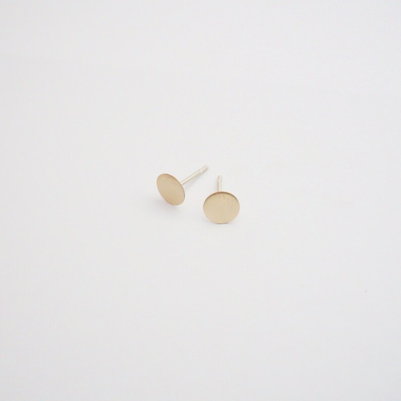 May include: A pair of gold-toned stud earrings with a circular design. The earrings are on a white background.