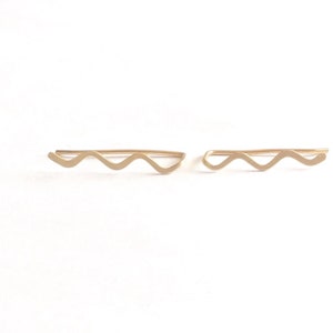 Könnte beinhalten: Ein Paar goldene Ohrclips mit einem wellenförmigen Design.