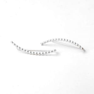 May include: A pair of silver ear cuffs with a curved design. The cuffs are made of small, round beads.