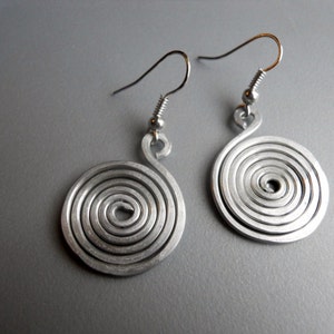 May include: A pair of silver spiral earrings with a simple design. The earrings are made of metal wire that is twisted into a spiral shape. The earrings are about 1 inch in diameter.