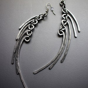 May include: A pair of silver earrings with a chain and multiple curved metal pieces hanging from each earring.