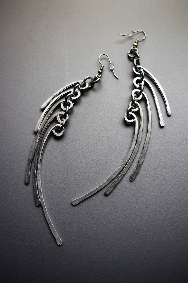 May include: A pair of silver earrings with a chain and multiple curved metal pieces hanging from each earring.