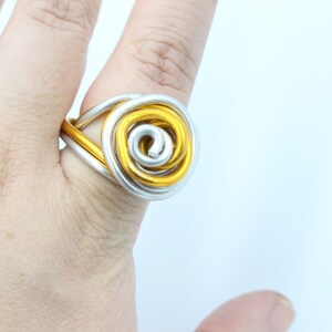May include: A gold and silver wire ring with a spiral design. The ring is worn on a finger.