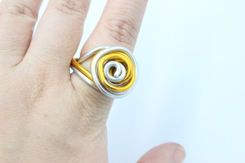 May include: A gold and silver wire ring with a spiral design. The ring is worn on a finger.
