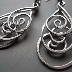 May include: A pair of silver dangle earrings with a swirling, abstract design. The earrings are made of metal wire and have a hammered finish.