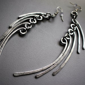May include: A pair of silver earrings with a geometric design. The earrings are made of multiple thin metal strips that are curved and joined together. The earrings are long and dangle.