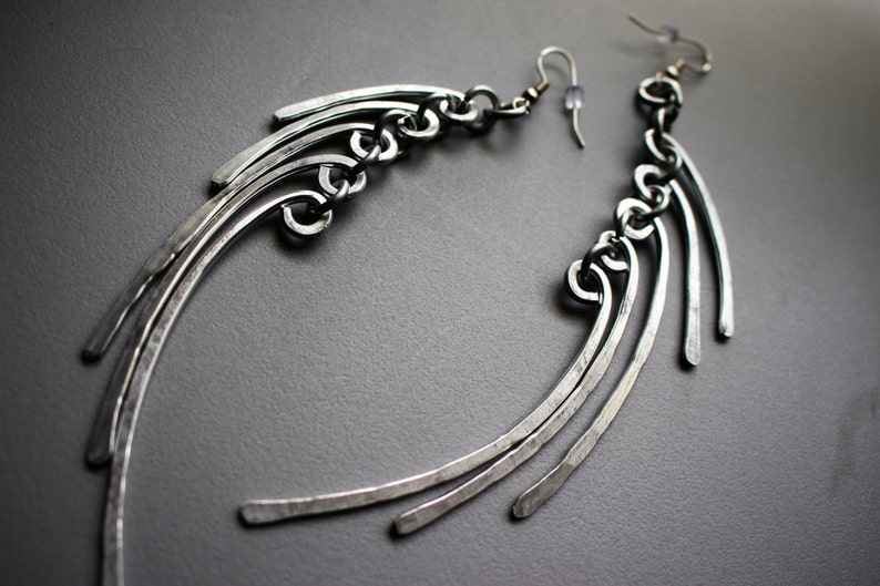 May include: A pair of silver earrings with a geometric design. The earrings are made of multiple thin metal strips that are curved and joined together. The earrings are long and dangle.