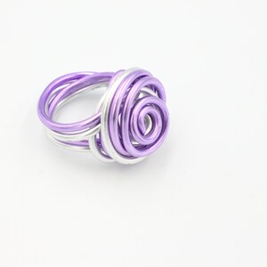 May include: A purple and silver wire ring with a spiral design. The ring is made of wire that has been twisted and shaped into a rose-like design.