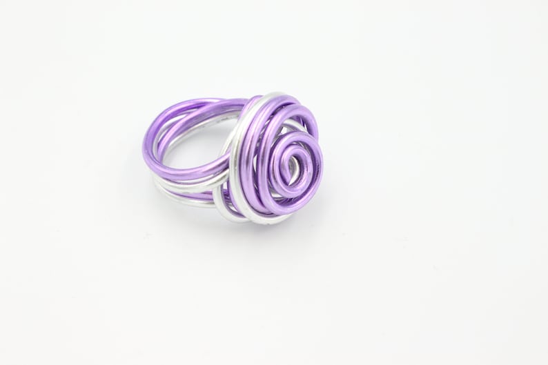 May include: A purple and silver wire ring with a spiral design. The ring is made of wire that has been twisted and shaped into a rose-like design.