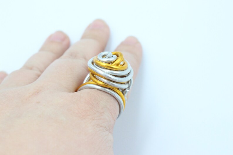 May include: A gold and silver wire ring with a unique, twisted design. The ring is large and appears to be handmade.