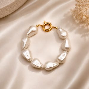 May include: A bracelet featuring irregular, teardrop-shaped white faux pearls strung together, secured with a polished gold-tone circular toggle clasp. The pearls have a smooth, glossy finish and are arranged in a continuous circular loop.