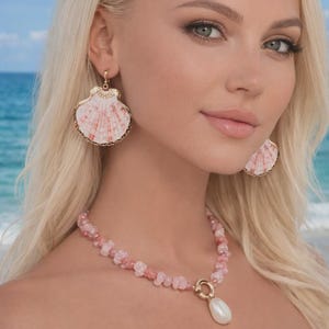 Op de afbeelding: Een sieradenset met schelpmotief met een ketting en oorbellen. De oorbellen en de hanger van de ketting zijn gevormd als schelpen met roze en witte patronen, omlijst met goudkleurig metaal. De ketting is gemaakt van roze kralen en heeft een witte parel hanger.