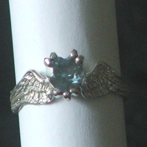May include: A silver ring with a blue gemstone in the center and two wings on either side.