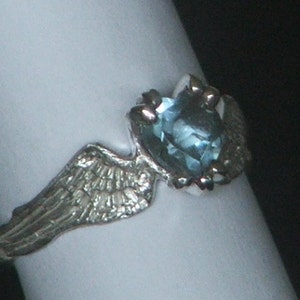 May include: A silver ring with a light blue gemstone set in a wing design.