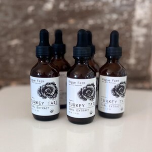 May include: Four brown glass bottles with black dropper tops and white labels. The labels say "Rogue Farm" and "Turkey Tail Dual Extract" with a mushroom illustration.