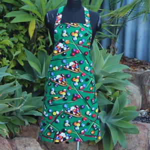 May include: A green apron with a pool table print featuring billiard balls and cues. The apron has adjustable straps and a large pocket.