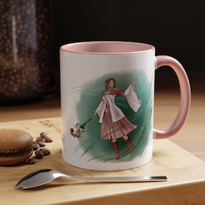 Könnte beinhalten: Weiße Keramik-Tasse mit rosa Innenraum und Henkel. Die Tasse zeigt eine Fantasy-Illustration einer Frau in einem rosa-weißen Kleid, die einen Stab hält. Der Hintergrund ist grün mit weißen Akzenten.