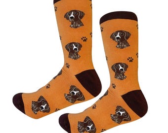 May include: A pair of orange socks with a brown and white German Shorthaired Pointer dog pattern. The socks have a brown cuff and a brown heel and toe.
