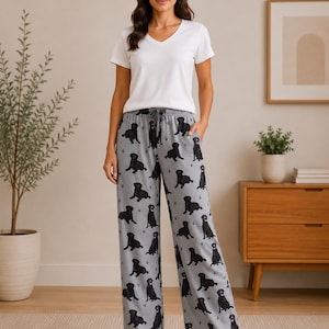 May include: A white V-neck short-sleeve t-shirt paired with grey lounge trousers featuring an all-over print of black Labrador retriever dogs and small paw prints. The trousers have a drawstring waistband and side pockets for a relaxed fit.