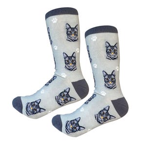 Op de afbeelding: Een paar grijze sokken met een patroon van grijze kattengezichten en witte potafdrukken. De sokken hebben een donkergrijze boord.