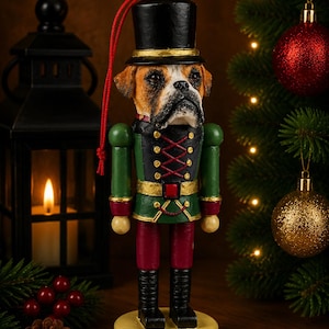 Può includere: Un ornamento schiaccianoci a forma di cane Boxer che indossa un cilindro nero e un'uniforme in stile militare verde, nera e rossa. La figura poggia su una base rotonda gialla e include un cordino rosso attaccato alla parte superiore del cappello.