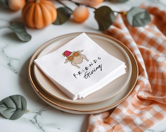 May include: White paper napkins with a cartoon turkey wearing sunglasses and a red fez. The napkins are stacked on a beige plate and say "F.R.I.E.N.D.S. Giving" in black text.
