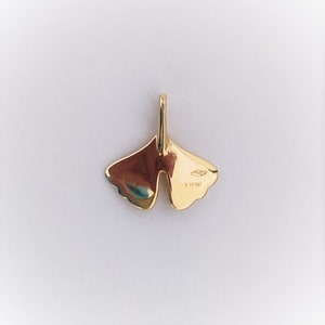 May include: A gold pendant in the shape of a ginkgo leaf. The back of the pendant has a hallmark that reads "925 750 18K".