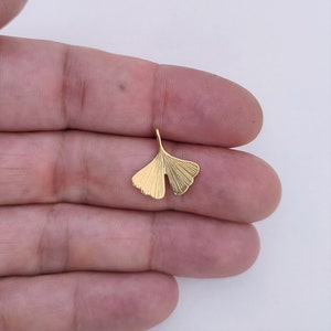May include: A gold-coloured ginkgo leaf pendant charm. The leaf is detailed with veins and has a smooth, polished finish.
