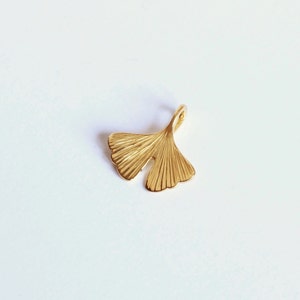 May include: A gold-coloured ginkgo leaf charm pendant. The leaf is detailed with fine lines and has a loop at the top for attaching to a chain or bracelet.