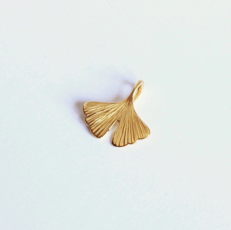 May include: A gold-coloured ginkgo leaf charm pendant. The leaf is detailed with fine lines and has a loop at the top for attaching to a chain or bracelet.
