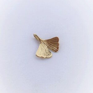 May include: A gold-coloured ginkgo leaf charm pendant. The leaf is detailed with veins and has a smooth, polished finish.