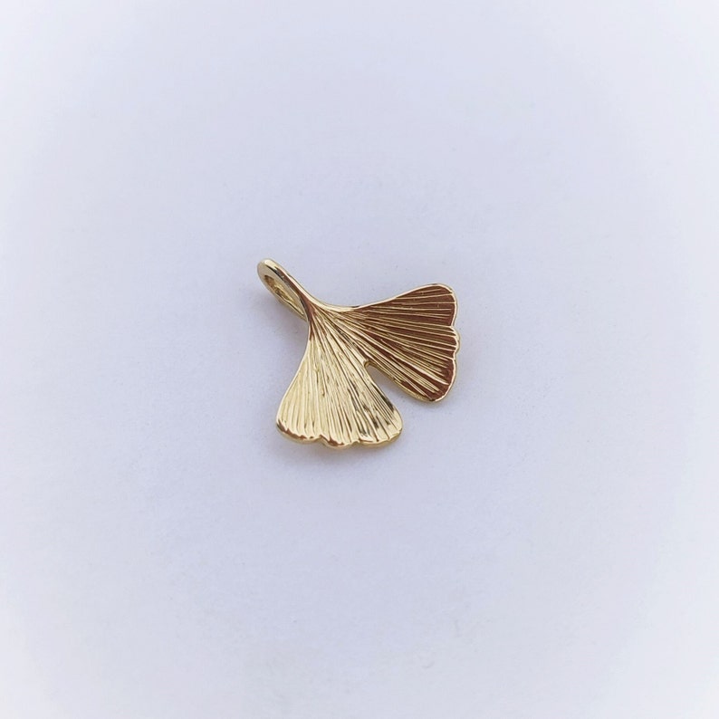 May include: A gold-coloured ginkgo leaf charm pendant. The leaf is detailed with veins and has a smooth, polished finish.