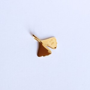 May include: A gold-coloured ginkgo leaf pendant charm. The back of the charm has a small marking that reads "925".