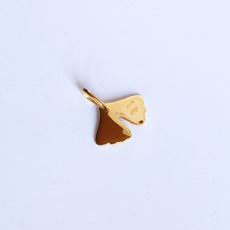 May include: A gold-coloured ginkgo leaf pendant charm. The back of the charm has a small marking that reads "925".