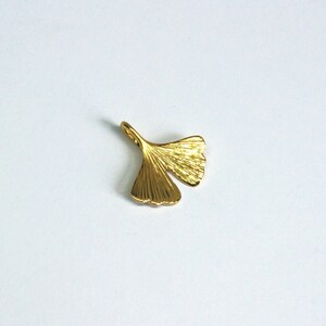 May include: A gold-coloured ginkgo leaf charm pendant. The leaf is detailed with veins and has a loop at the top for attaching to a necklace or bracelet.