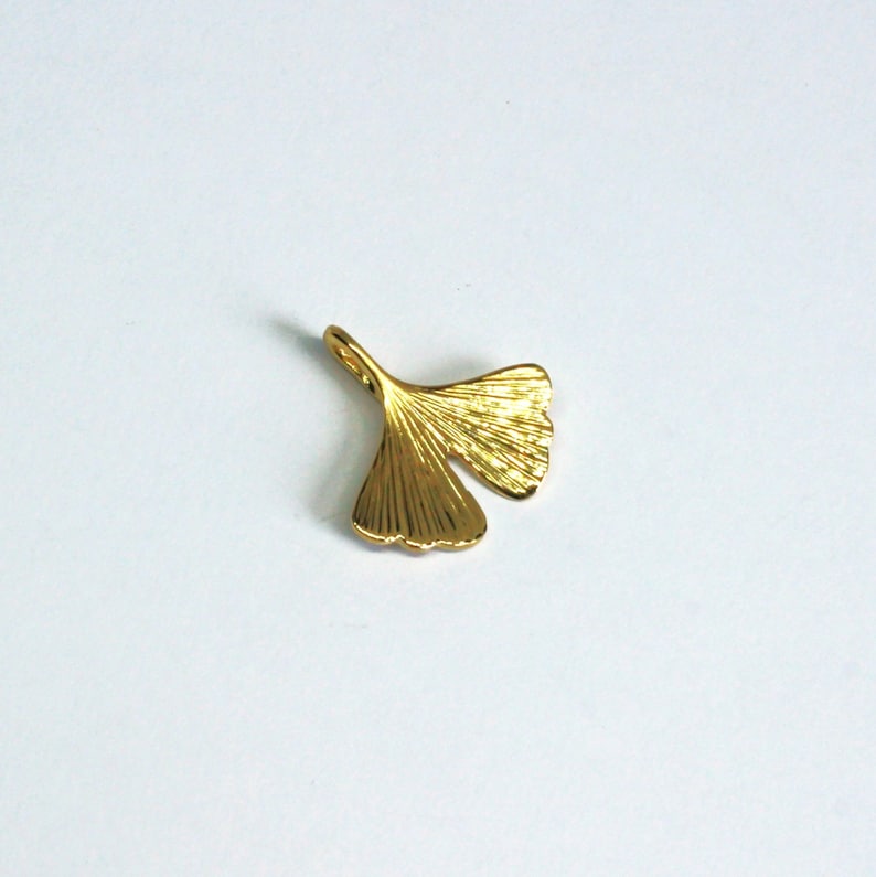 May include: A gold-coloured ginkgo leaf charm pendant. The leaf is detailed with veins and has a loop at the top for attaching to a necklace or bracelet.