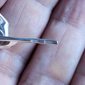May include: A silver-colored metal earring post featuring two distinct hallmarks stamped into the surface. The first oval stamp contains the number 925, while the second rectangular stamp displays the alphanumeric text 270 FC, indicating the metal purity.
