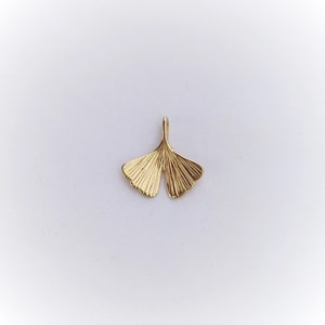 May include: A gold-coloured ginkgo leaf pendant charm. The leaf is detailed with veins and has a smooth, polished finish.